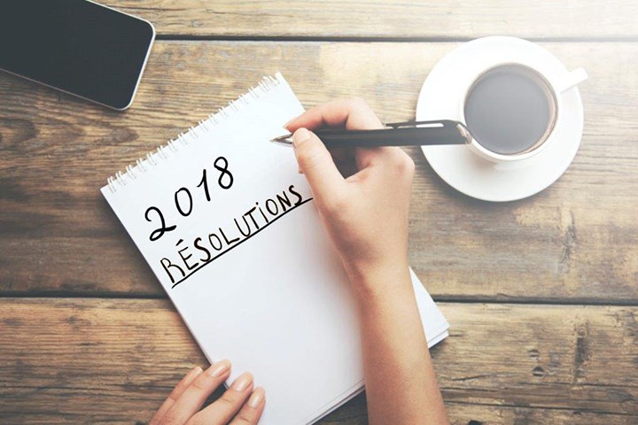 Une femme écrit les mots « Résolutions de 2018 » sur une tablette de papier placée près d’une tasse de café et d’un téléphone intelligent.